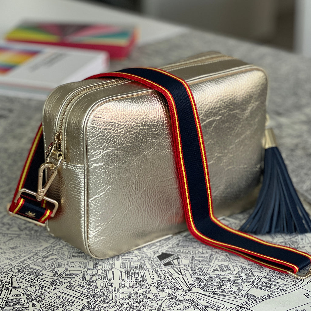 Large gold crossbody bag with interchangeable navy, red and yellow fabric strap with navy blue large tassel all with gold hardware 