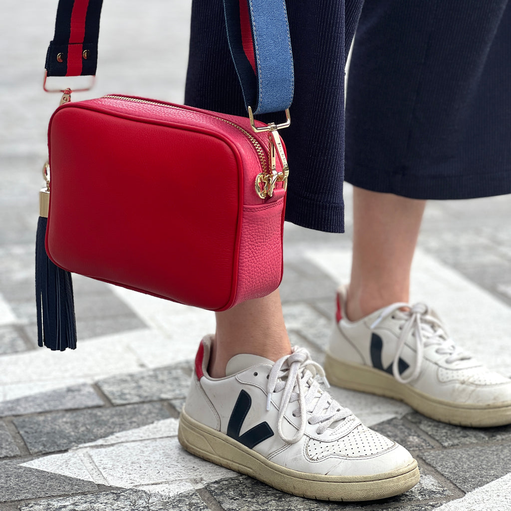 Red and Pink leather crossbody camera style bag with denim strap,  next to trainers