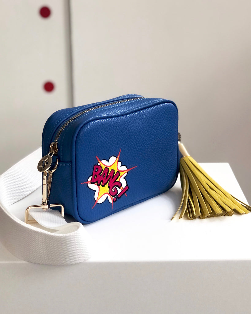 Small blue leather crossbody bag with white fabric strap and yellow large removable leather tassel 