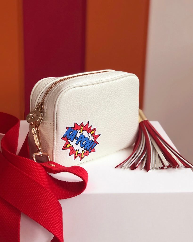 White small leather handbag with graphic ka-pow design with red slim fabric strap and red and white large leather removable tassel 