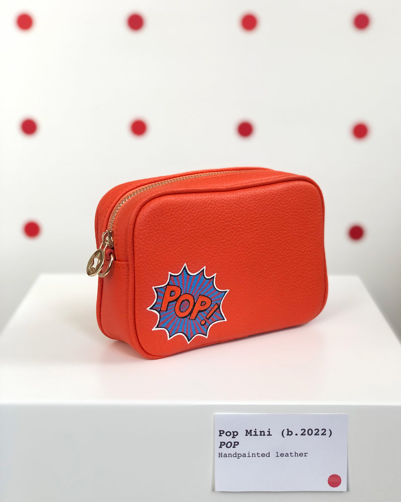 Small orange leather cross body bag with graphic painting in the corner of the bag all with gold hardware